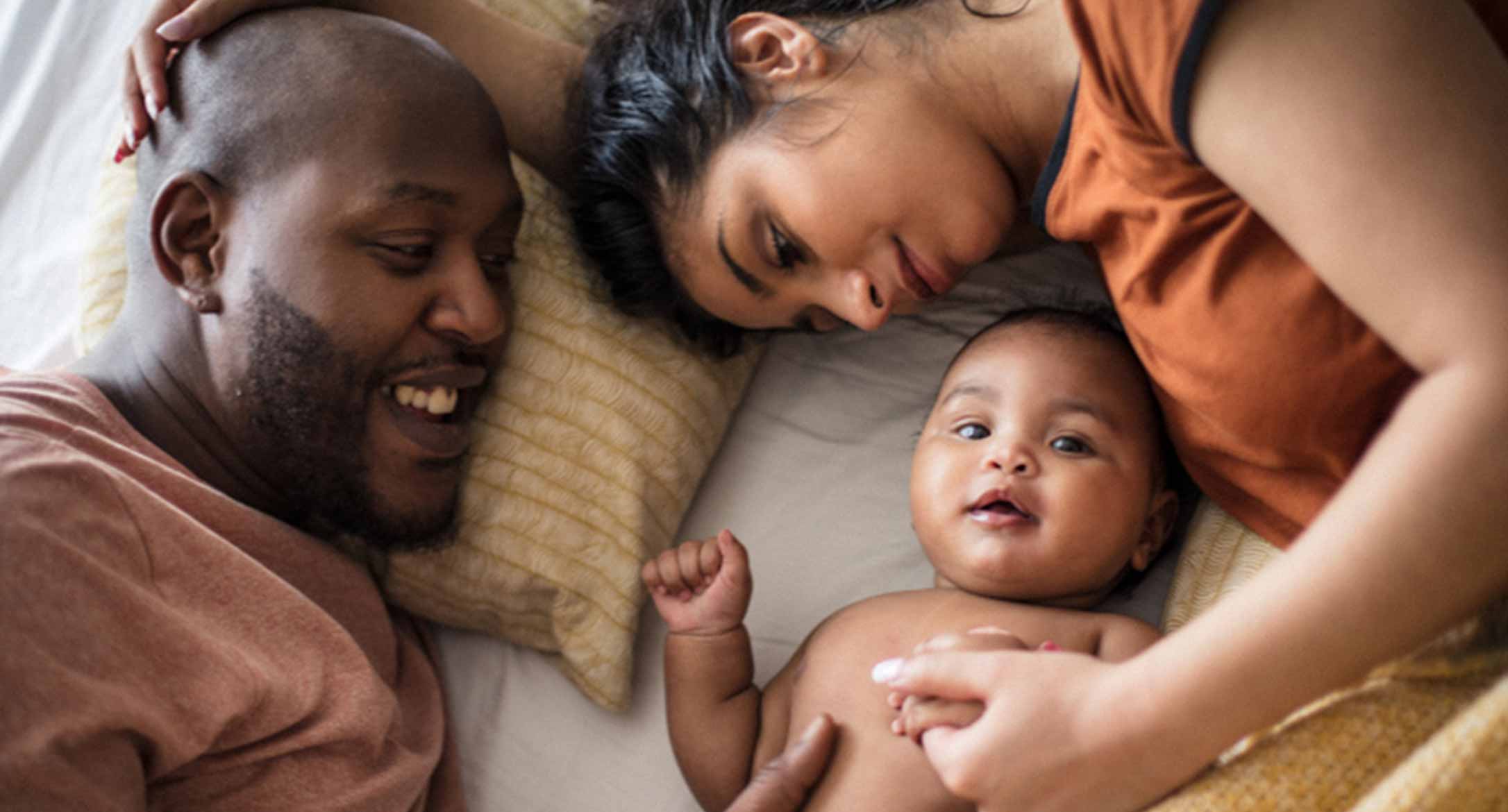 Un papa et une maman allongés sur le lit avec leur nouveau-né.